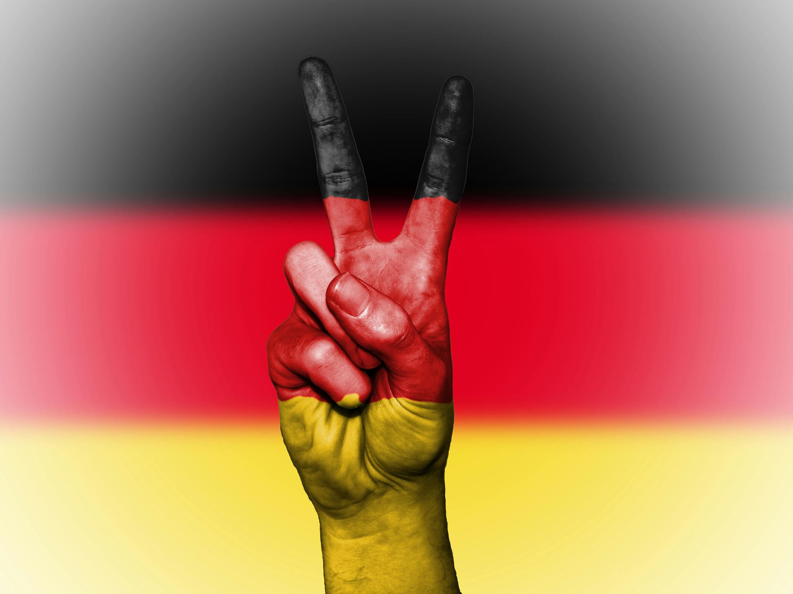 Hand showing a peace sign painted with the German flag colors, symbolizing peace and unity.