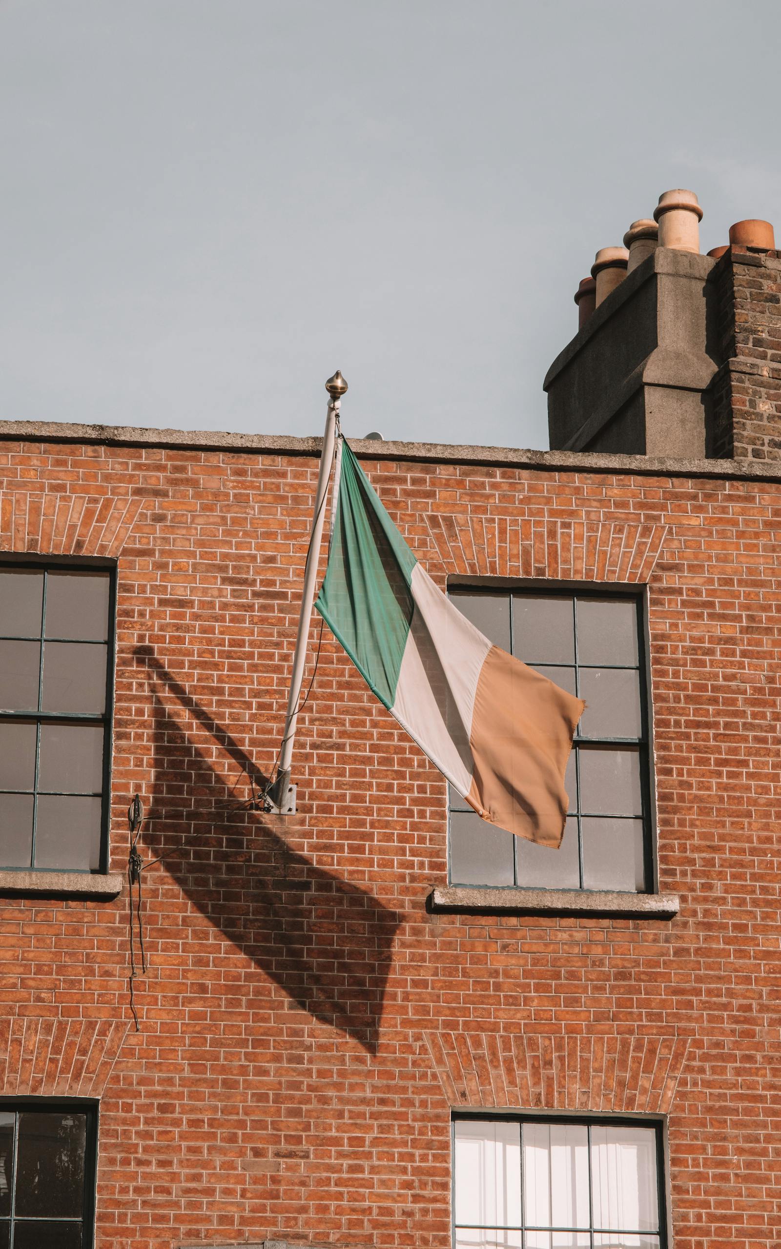The Irish flag waves on a brick building facade in Dublin, Ireland.